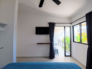 Une chambre avec un lit, un téléviseur fixé au mur, une porte-fenêtre coulissante donnant sur un balcon et un ventilateur de plafond.