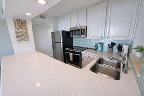 A modern kitchen with white cabinets, stainless steel appliances, a granite countertop, and a backsplash with blue mosaic tiles. - Gulf-Front Sandestin Studio | Balcony Views, Pool & Beach Access | Beachside II 4268 (Miramar Beach)
