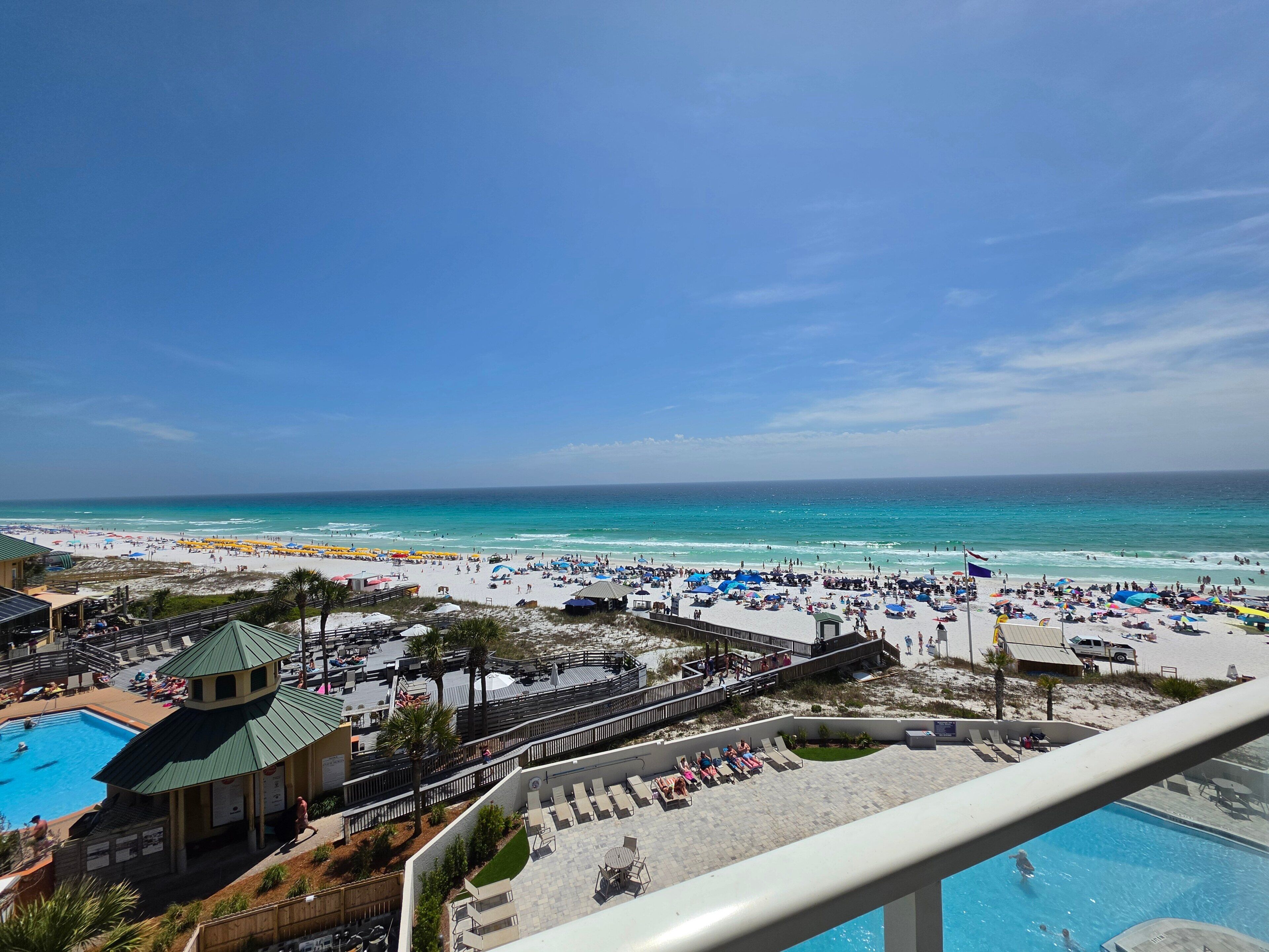 A beach resort with a pool, beach umbrellas, and a view of the ocean.