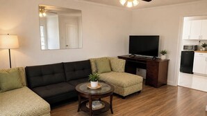A living room with a sofa, a coffee table, a TV, and a kitchen area with cabinets and appliances.