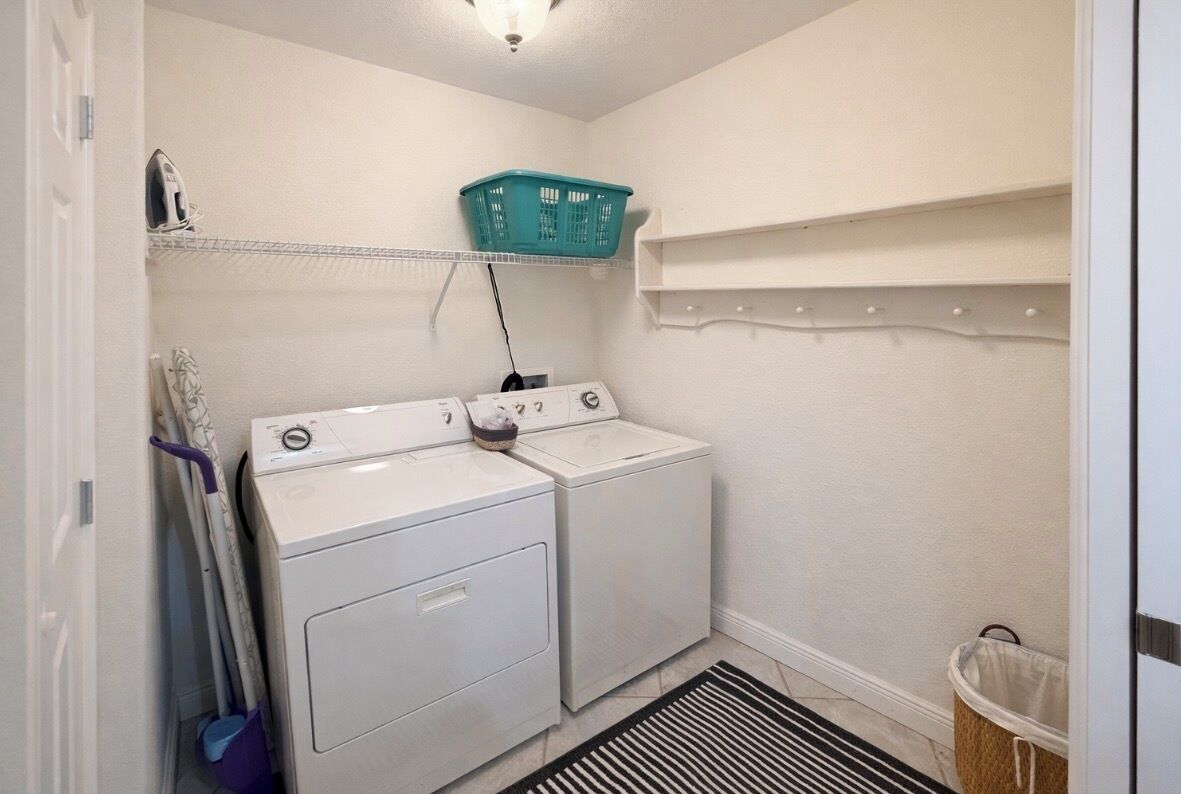 Una sala de bugaderia amb dues rentadores i assecadores blanques, una cistella de roba teulada sobre una estantalia i un cubell de brossa blanc.