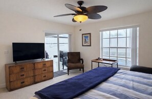 Une chambre à coucher avec un lit, un téléviseur posé sur une commode en bois, un ventilateur de plafond et une fenêtre donnant sur un paysage agréable.