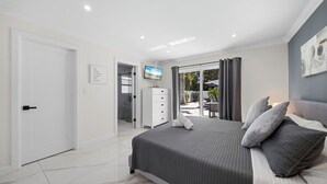 Een moderne slaapkamer met een groot bed, een televisie, een kledingkast en een schuifdeur van glas naar een buitenruimte.