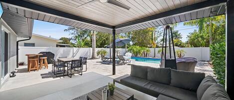 Um alpendre coberto com ventilador de teto, móveis de exterior, piscina e vista para o quintal.