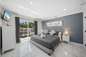 Une chambre moderne dotée d’un grand lit, d’un téléviseur à écran plat, d’une table de chevet et donnant sur un espace extérieur grâce à une porte vitrée.