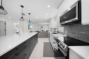 Une cuisine moderne dotée d’un grand îlot central, de meubles de rangement noirs et blancs, d’appareils électroménagers en acier inoxydable et de luminaires suspendus.
