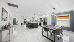 Een moderne keuken met een centraal eiland, een eethoek met tafel en stoelen, en een groot raam met uitzicht.