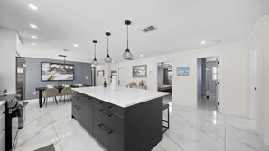 Een moderne keuken met een groot schiereiland, hangende lampen en een eethoek met stoelen.
