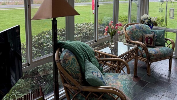 A conservatory with wicker furniture, a table, and a TV. - Relax & Recharge at the Northern Gateway – Lakeview Retreat in Rouses Point, NY (Rouses Point)