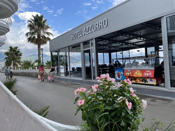 A hotel named 'HOTEL AZZURRO' with a covered outdoor seating area, palm trees, and a view of the sea. - Azzurro Hotel Bijela, Herceg Novi (Bijela)