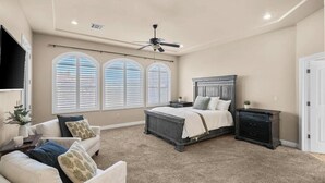 A bedroom with a bed, a ceiling fan, a nightstand, a dresser, and a TV mounted on the wall. - Enjoyable 5 bedroom house with community pool (Las Cruces)