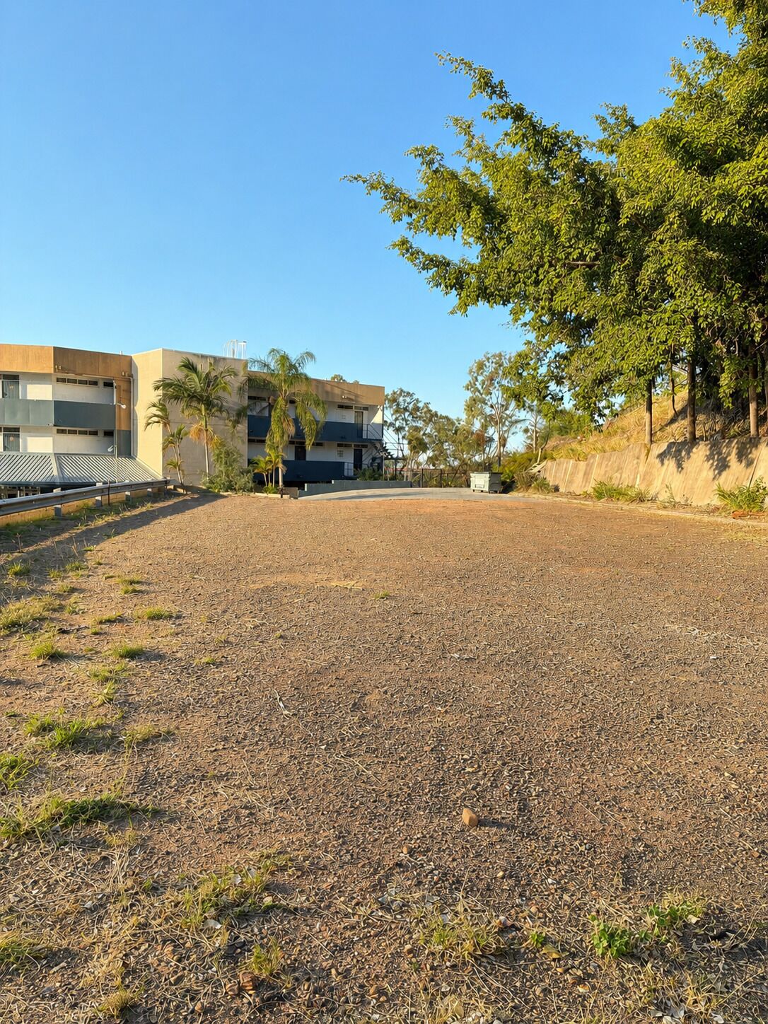 A gravel sports field with a building in the background.