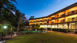 A multi-story hotel with a swimming pool, surrounded by a well-maintained lawn and palm trees. - Lumina Motel (South Gladstone)