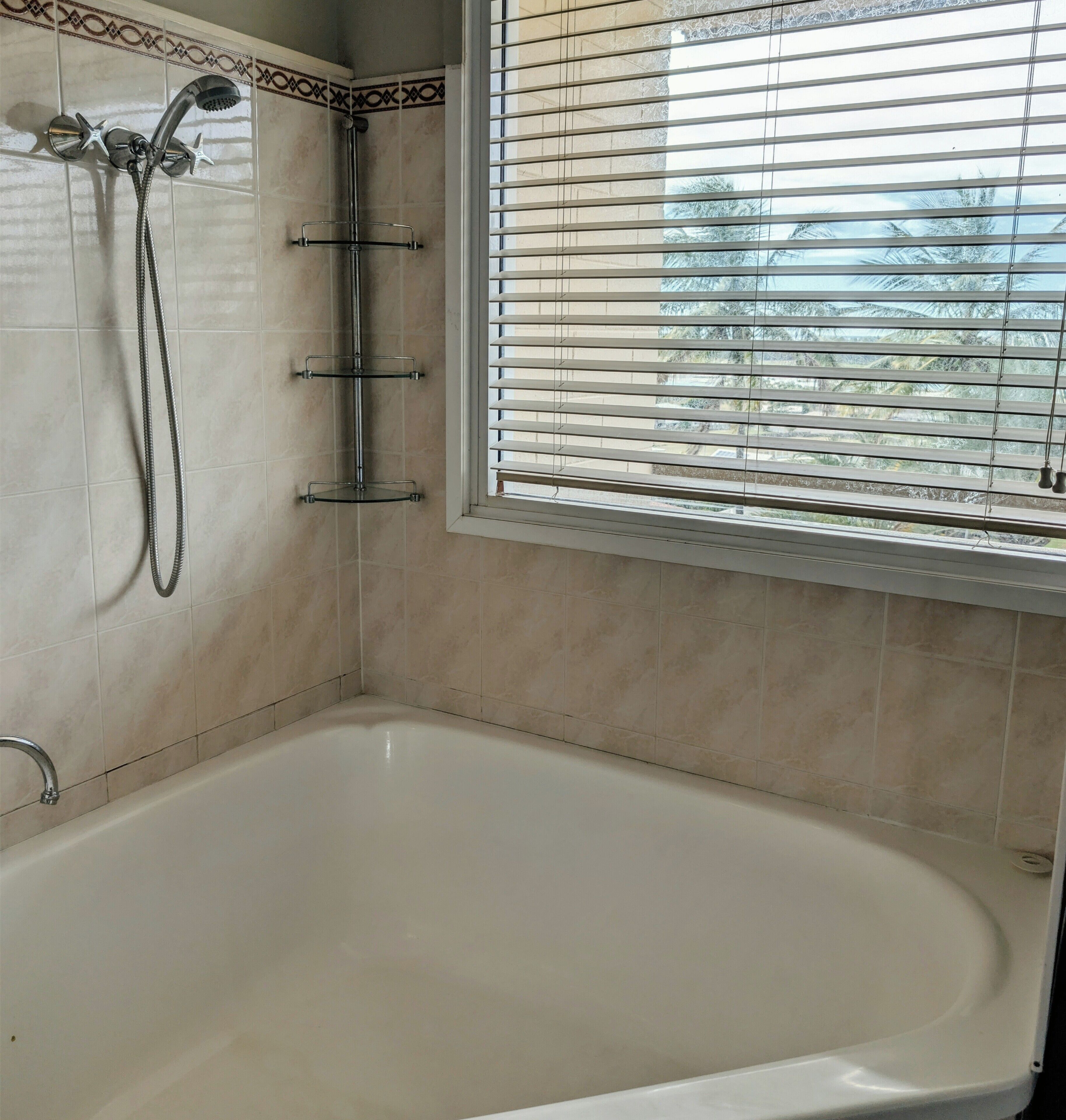 A bathroom with a bathtub, a shower, and a window with blinds.