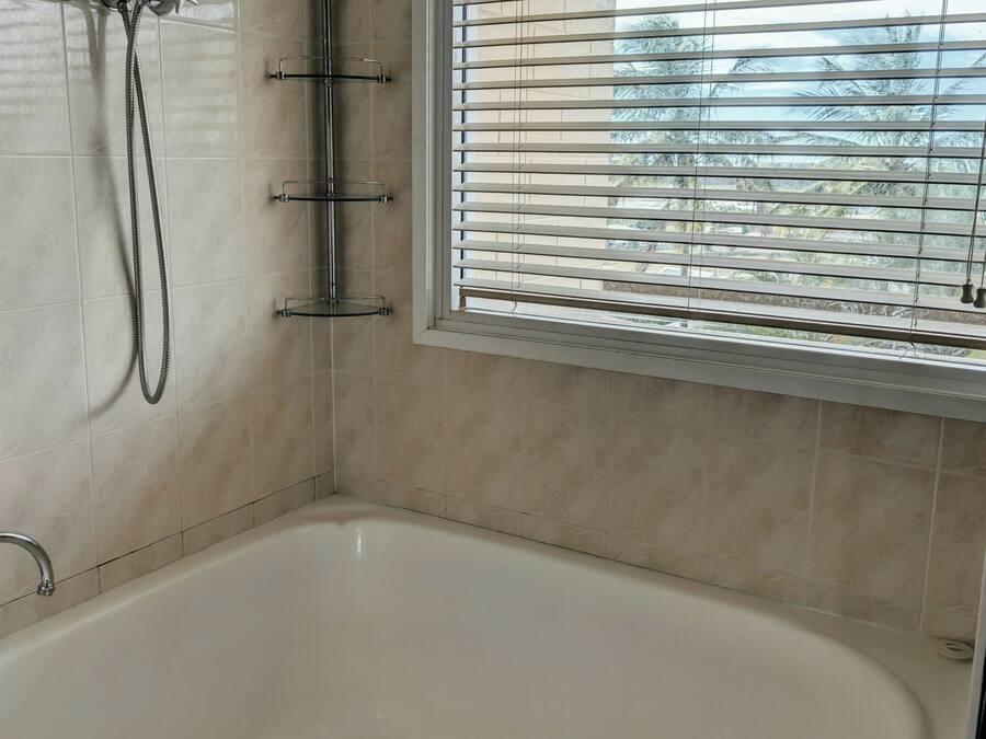 Een badkamer met een bad, een douche en een raam met jaloezieën.