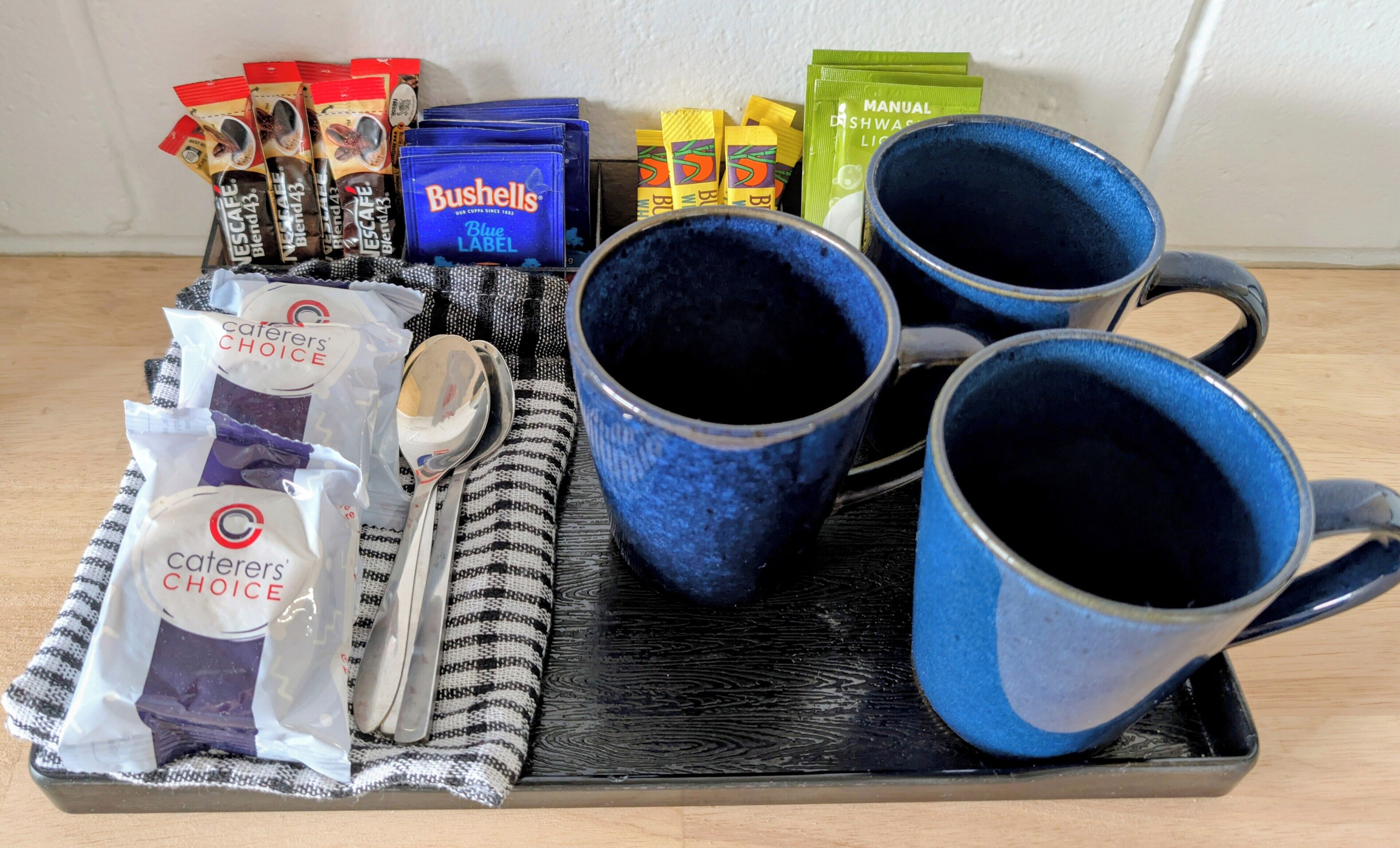 En bakke med kaffekapsler, en ske, en kop og en pose fløde.