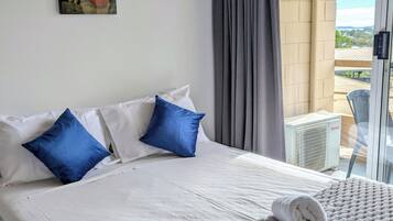 Ett hotellrum med en säng, kuddar, ett täcke, en handduk, ett fönster med gardiner och utsikt över omgivningen.