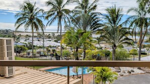 A balcony with a glass table and chairs, overlooking a swimming pool and palm trees. - Lumina Motel (South Gladstone)