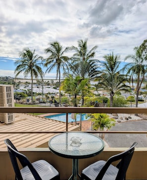 A balcony with a glass table and chairs, overlooking a swimming pool and palm trees. - Lumina Motel (South Gladstone)