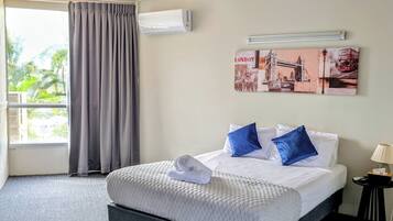 Een hotelkamer met een bed, een plafondventilator, een raam met gordijnen en een wandairconditioner.