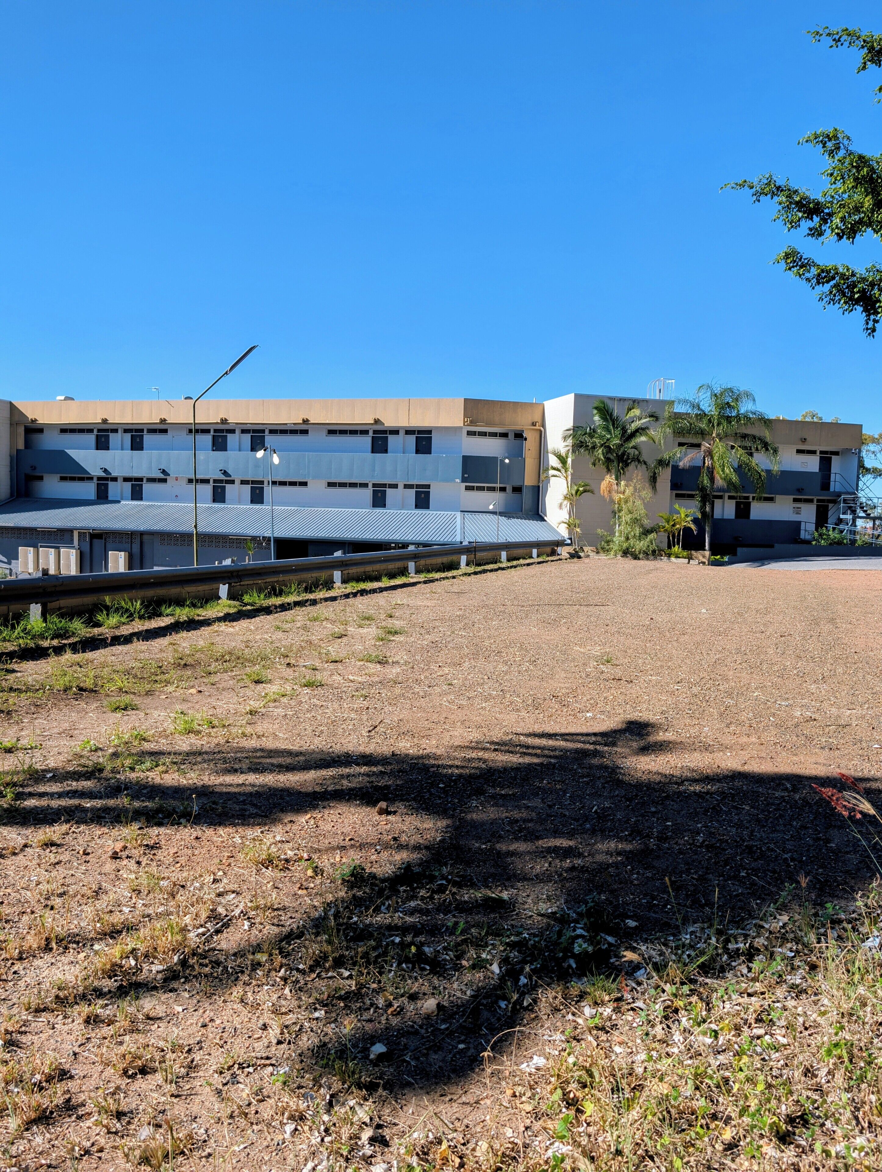 Um edifício com vários andares, um telhado plano e uma área de estacionamento na frente.