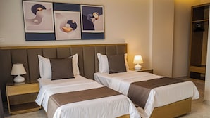 Een hotelkamer met twee bedden, een nachtkastje met een lamp, een aan de muur hangend kunstwerk en een spiegel.