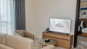 Een hotelkamer met een bank, een glazen salontafel, een televisie en een houten kast.