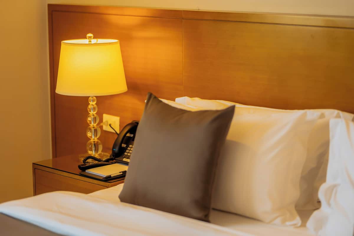 Ein Hotelzimmer mit Bett, Nachttischlampe, Telefon und Kissen.