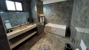 Een moderne badkamer met een grote spiegel, twee wastafels, een bad en een toilet.