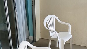 Dos sillas blancas de plástico en un balcón con un vidrio y una pared color beige.