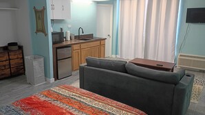 Un espacio habitable pequeño con kitchenette, un sofá, un tapete estampado y un televisor.