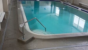 Una piscina interior con agua cristalina, un letrero de salida visible y una escalera que conduce a otra zona.