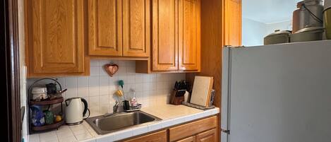 Une cuisine avec des meubles de rangement en bois, un plan de travail blanc, un évier et un réfrigérateur.
