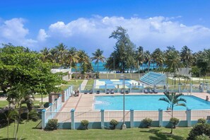 A pool area with multiple swimming pools, lounge chairs, and palm trees. - Luxury Apartment Luquillo | Ocean View Suite (Luquillo)