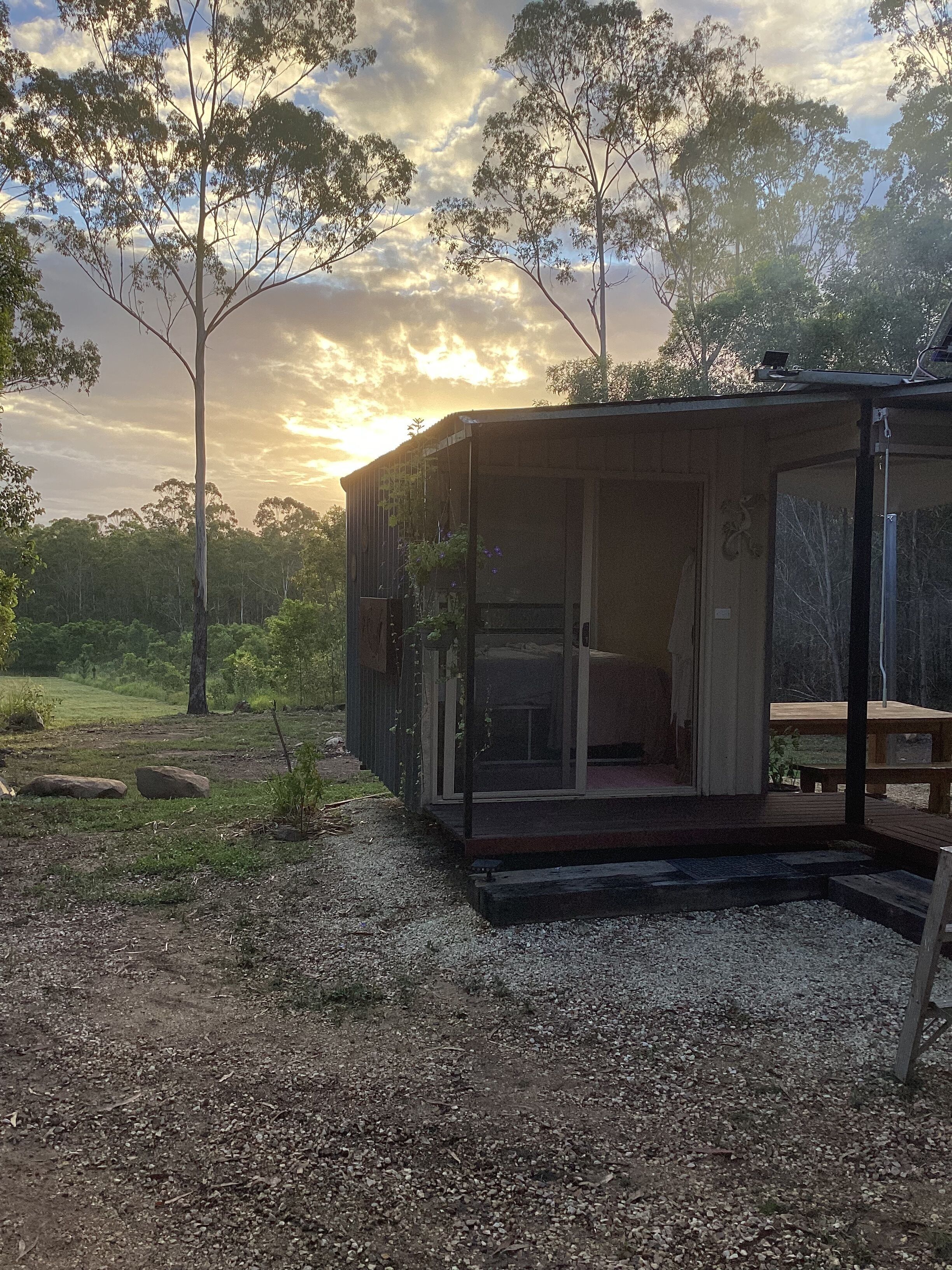 A rustic cabin with a glass door, surrounded by a gravel path and trees.
