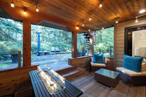 An outdoor wooden deck with a glass-top table, wicker furniture, and a bench. - Kinnikinnick Guest House (Ucluelet)