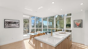 A modern kitchen with a large island, large windows, and a dining area with chairs.