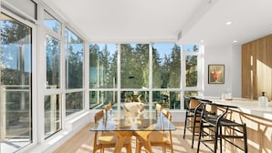 A modern kitchen with large windows, a glass dining table, and wooden chairs.