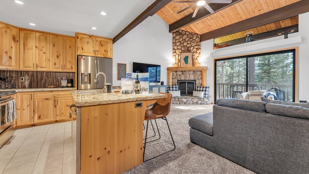 A modern kitchen with wooden cabinets, a central island, and a stone fireplace. - Alpine Pines | Deck | BBQ | Community Amenities (Kings Beach)
