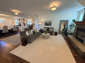 A spacious living room with a fireplace, a dining area, and a kitchen in the background.