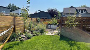 A backyard with a wooden fence, a hammock, and various plants and flowers. - The Blue House: Spacious home w/ patio, fenced yard, views, close to everything (Bozeman)