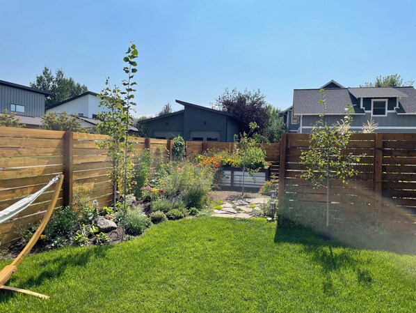 A backyard with a wooden fence, a hammock, and various plants and flowers.