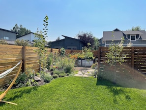 A backyard with a wooden fence, a hammock, and various plants and flowers.
