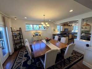 A spacious dining area with a wooden table, white chairs, and a chandelier.