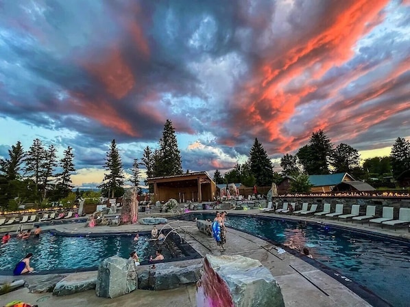A pool area with multiple pools, lounge chairs, and a wooden structure.