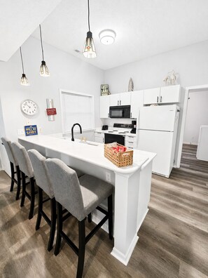 A modern kitchen with white cabinetry, a central island with bar stools, a microwave, stove, and refrigerator. - Spacious 3-bedroom condo on 1MM in brilliant Lake Ozark with AC (Lake Ozark)