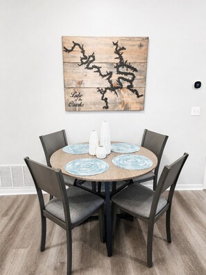 A dining area with a round table, four chairs, and a wall-mounted artwork depicting a tree branch. - Spacious 3-bedroom condo on 1MM in brilliant Lake Ozark with AC (Lake Ozark)