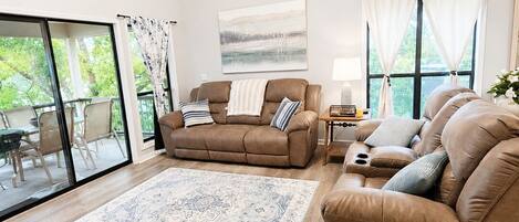 A spacious living room with a brown sofa, a coffee table, a large rug, and a ceiling fan.