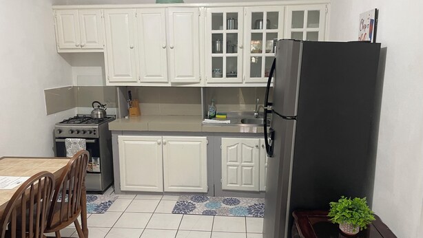 Une cuisine compacte avec des meubles blancs, un réfrigérateur noir, une cuisinière et un coin repas comprenant une table et des chaises.