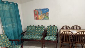 Une pièce comprenant un canapé, une table à manger avec des chaises, un tableau au mur et un rideau.